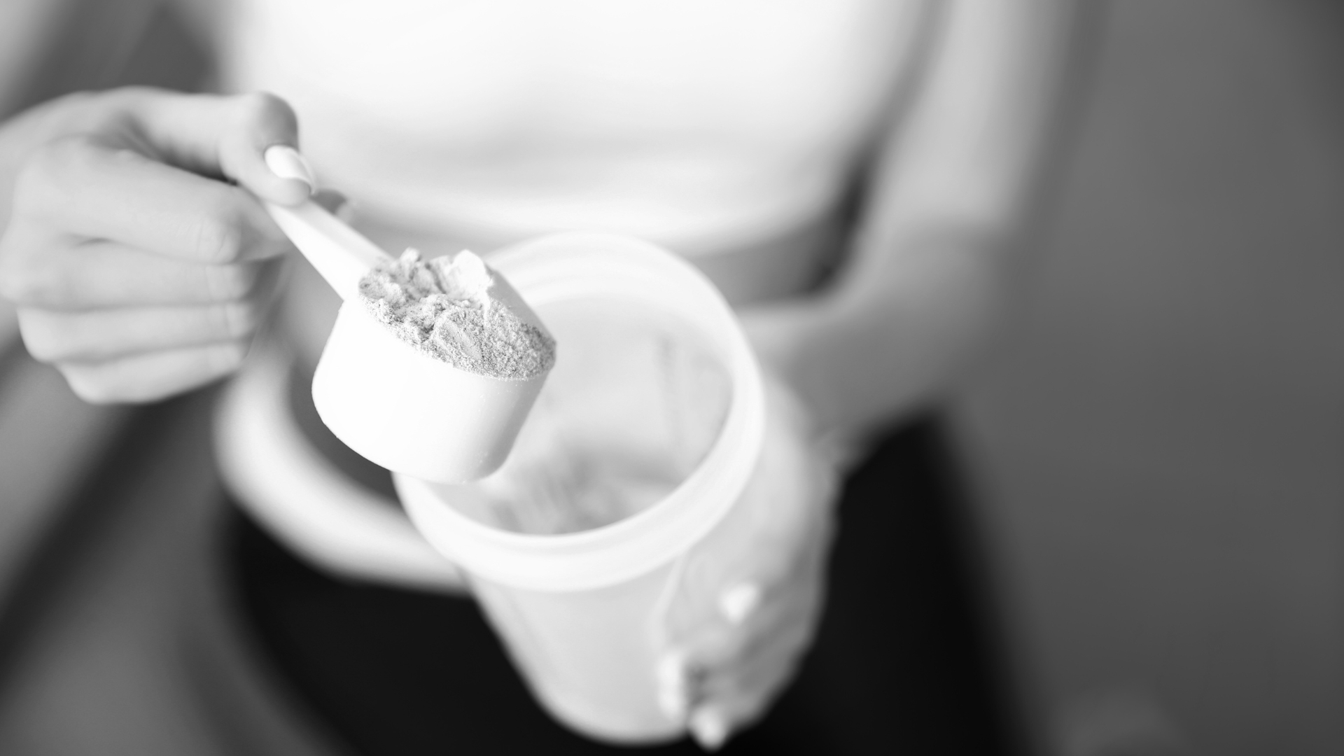 Close-up of a woman holding a scoop of protein powder over an open container, preparing a supplement shake.