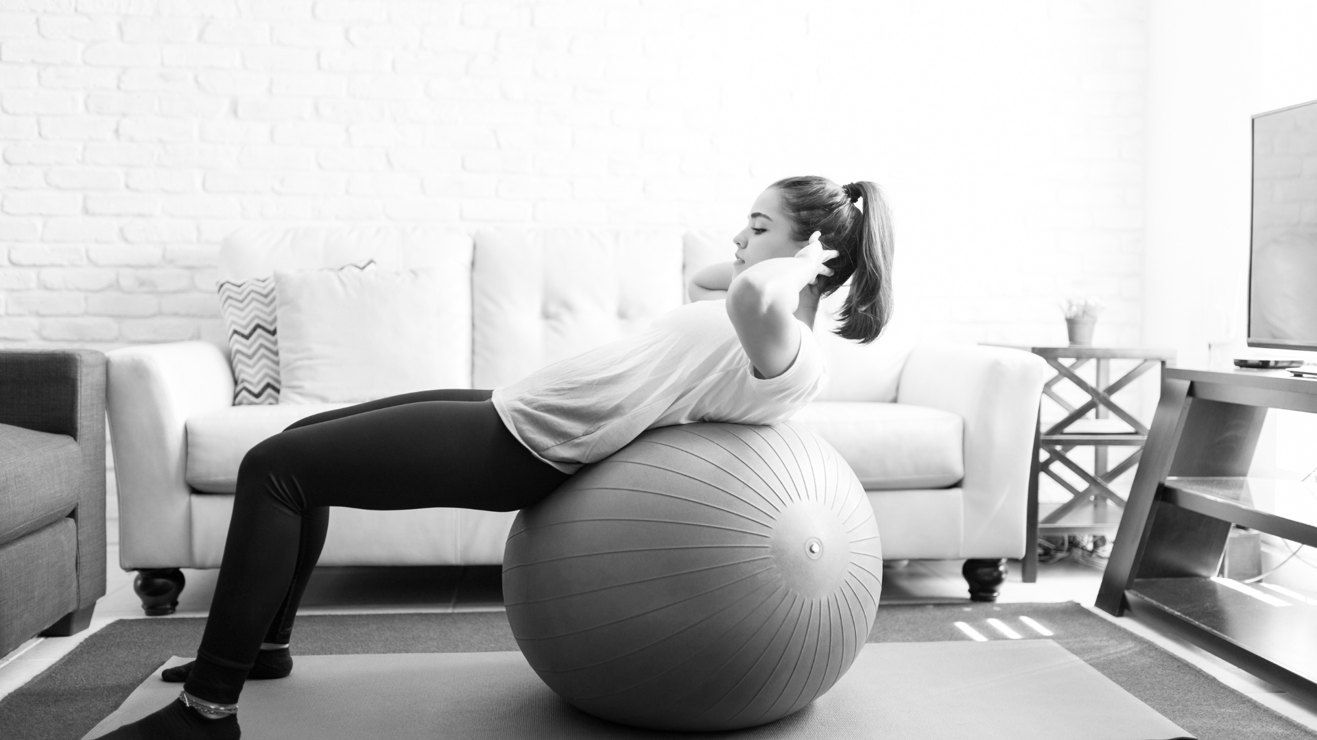 Woman performing a sit-up on a Swiss Ball in a home setting, engaging her core.