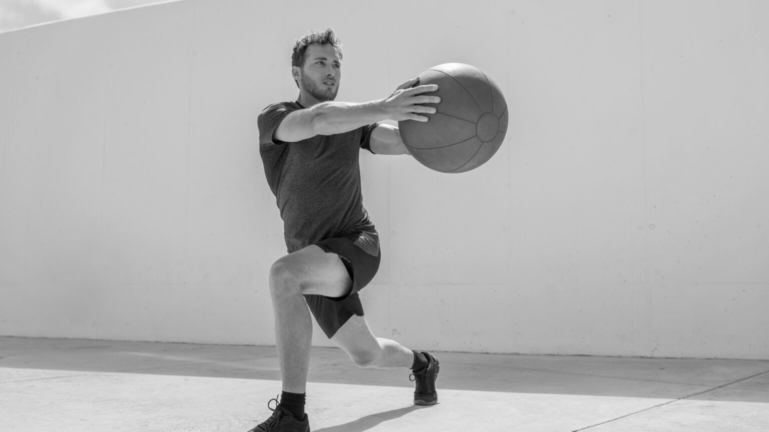 Male athlete performing a lunge with a medicine ball rotation, engaging core muscles.