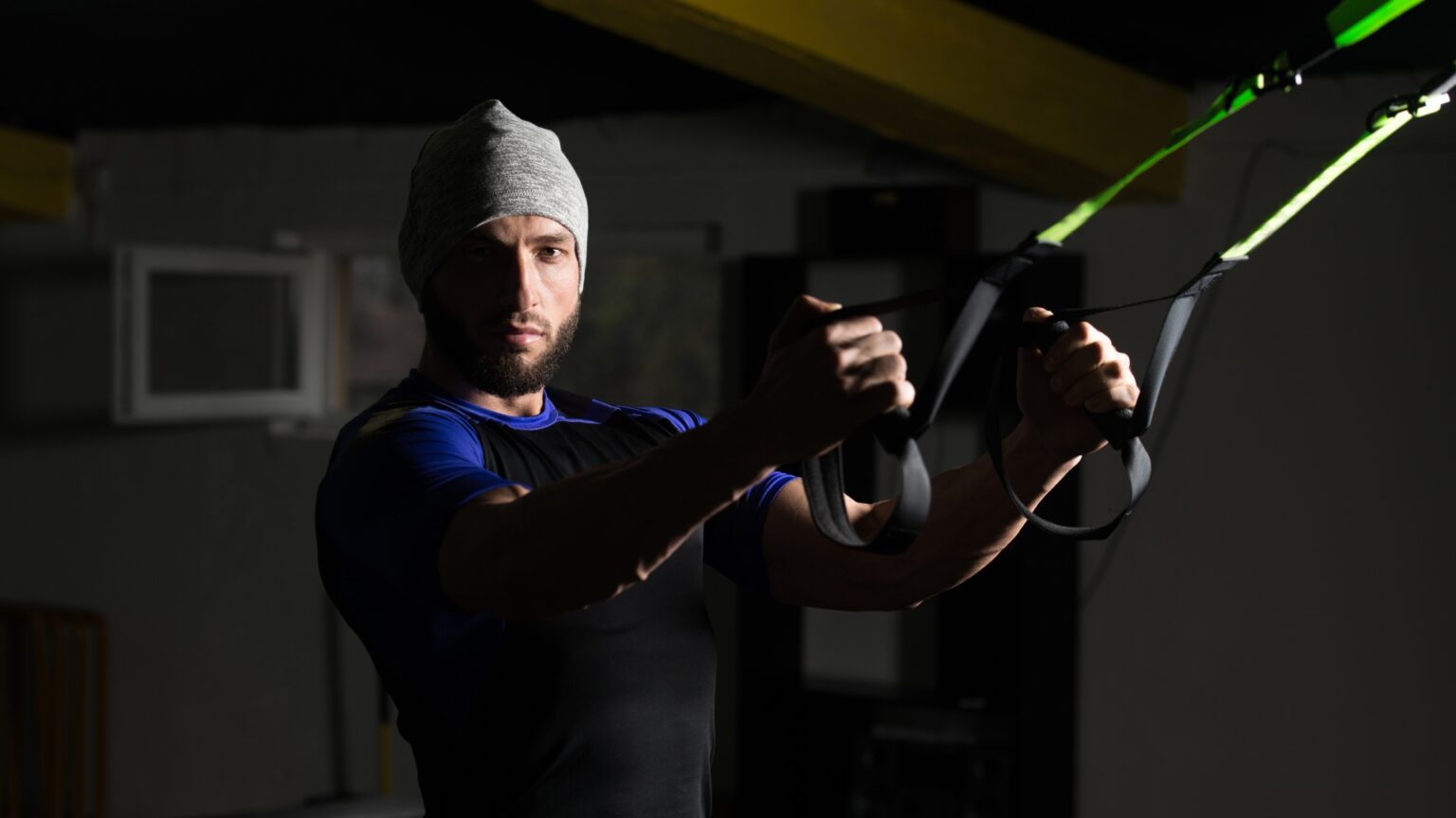 A focused man performing TRX rows in a dimly lit gym, working on back and grip strength.