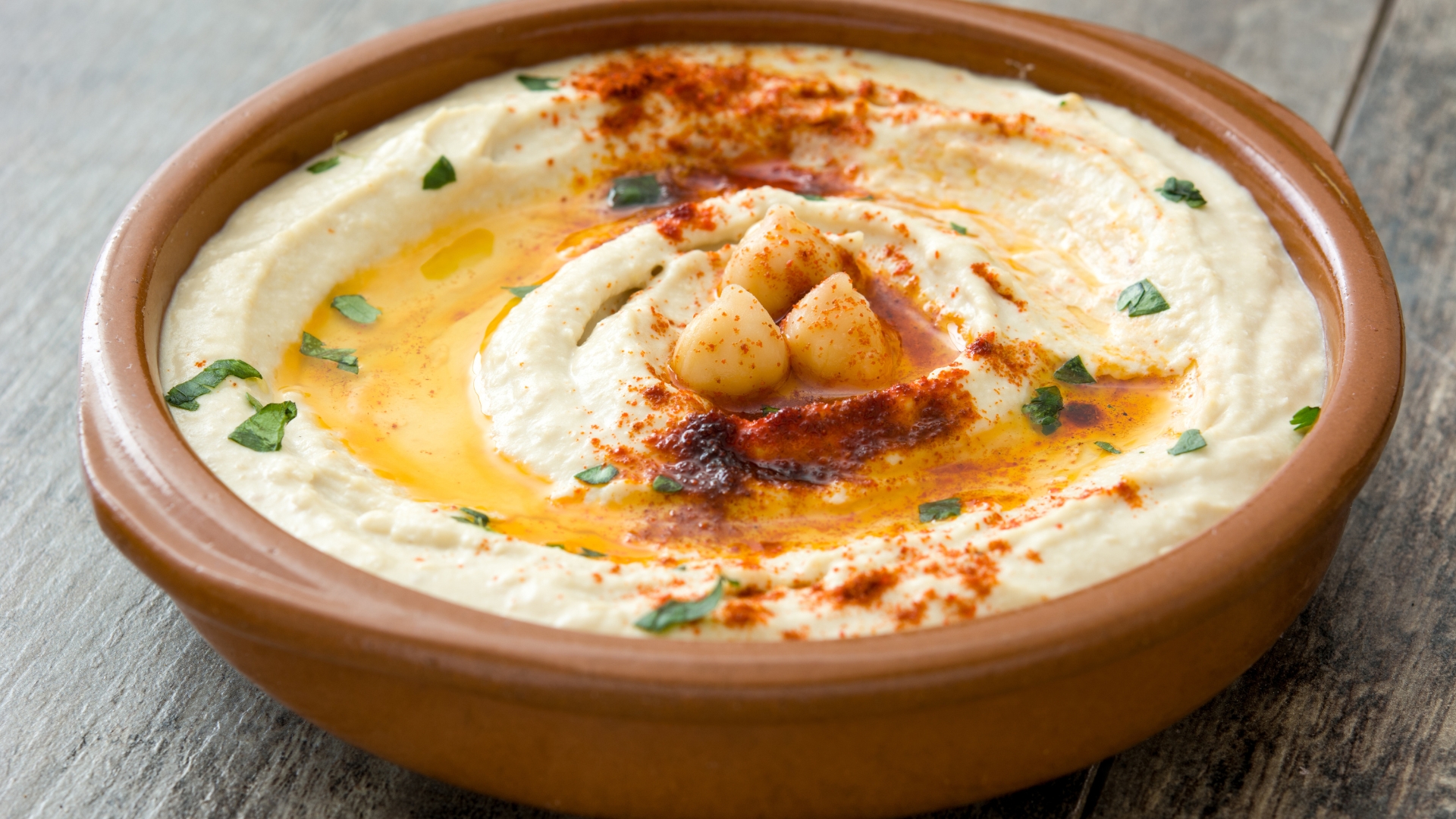 A bowl of hummus topped with olive oil, chickpeas, and paprika, garnished with parsley.