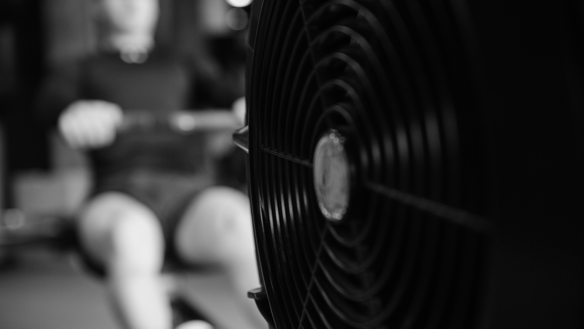 A close-up shot of an air bike fan, with an athlete rowing in the background, symbolizing endurance training.