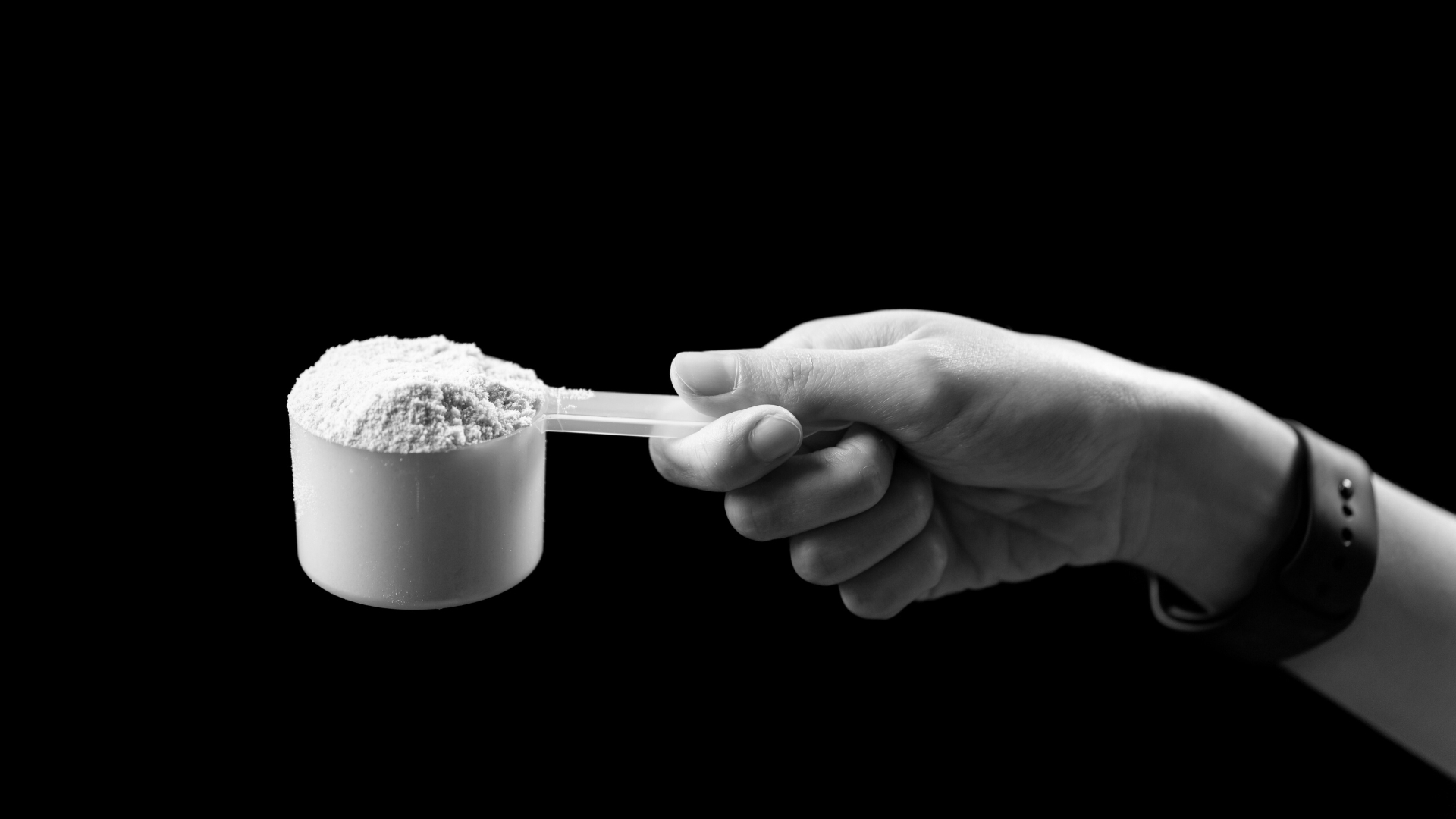 A hand holding a full scoop of protein powder against a dark background, symbolizing supplement intake and its role in fitness nutrition.