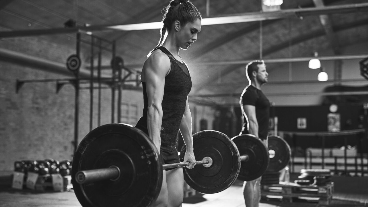 male and female athlete performing heavy barbell deadlifts in a gym, demonstrating strength training techniques for power and endurance.