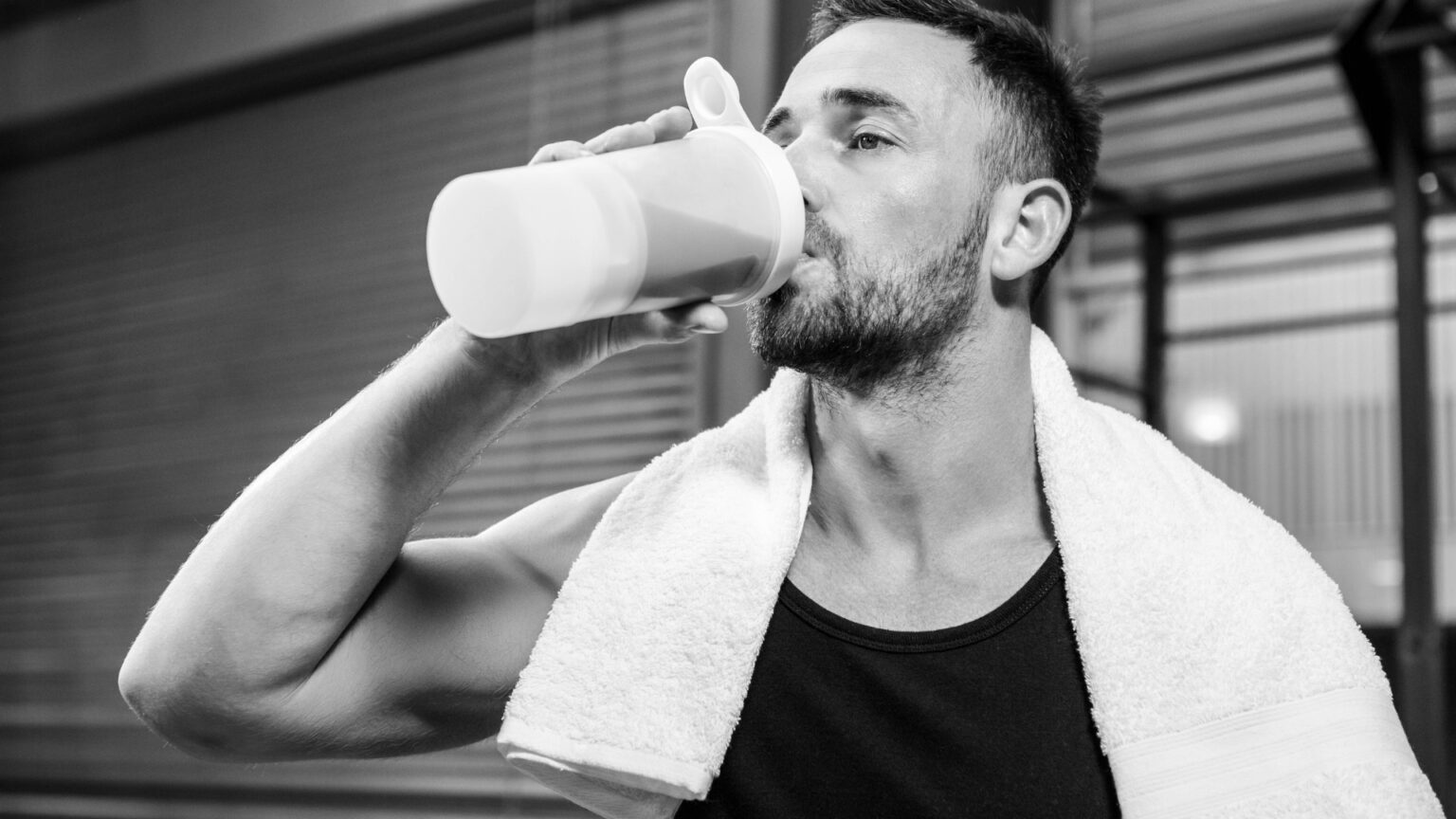 A fit male athlete in a gym drinking a protein shake after an intense workout, illustrating the role of supplements in muscle recovery.