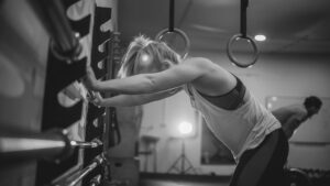  A woman resting against the gym wall after an intense workout, highlighting the effects of fasted cardio on energy levels, recovery, and muscle fatigue.