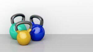  Three colorful kettlebells of different weights placed on a gym floor, representing progression and variety in kettlebell training.