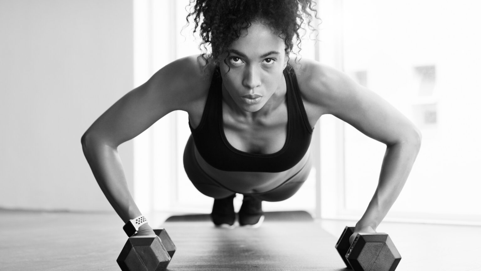 A focused woman performing push-ups on dumbbells, representing strength training combined with fasted cardio for fat loss and endurance.