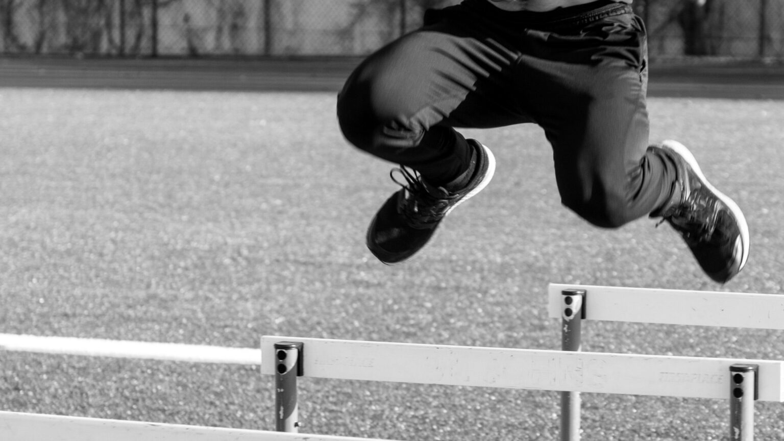 Athlete performing a hurdle jump on a track, demonstrating plyometric training for explosive power and agility.