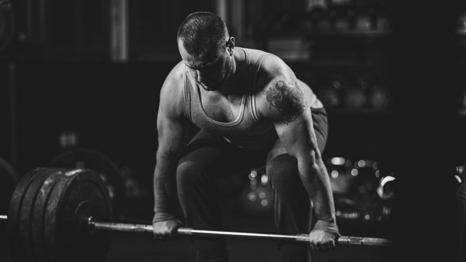 A muscular man performing a heavy deadlift in a dimly lit gym, demonstrating strength and dedication to training.