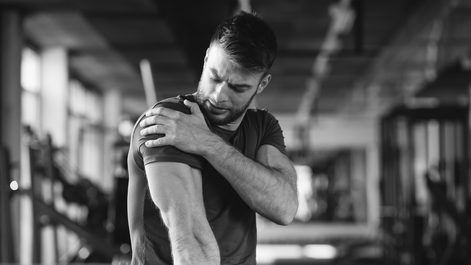 Man holding his shoulder in pain inside a gym, highlighting the need for shoulder recovery techniques.