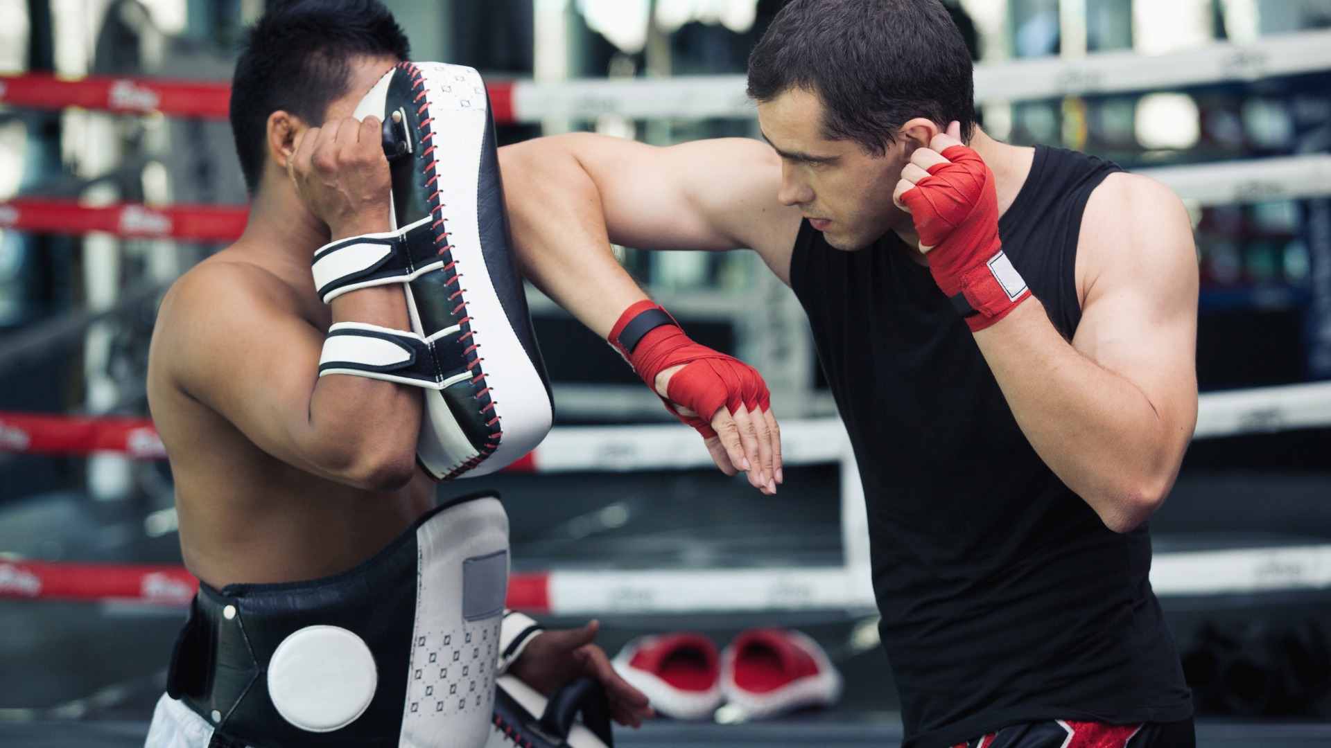 A Muay Thai fighter performing an elbow strike during pad training in a gym.