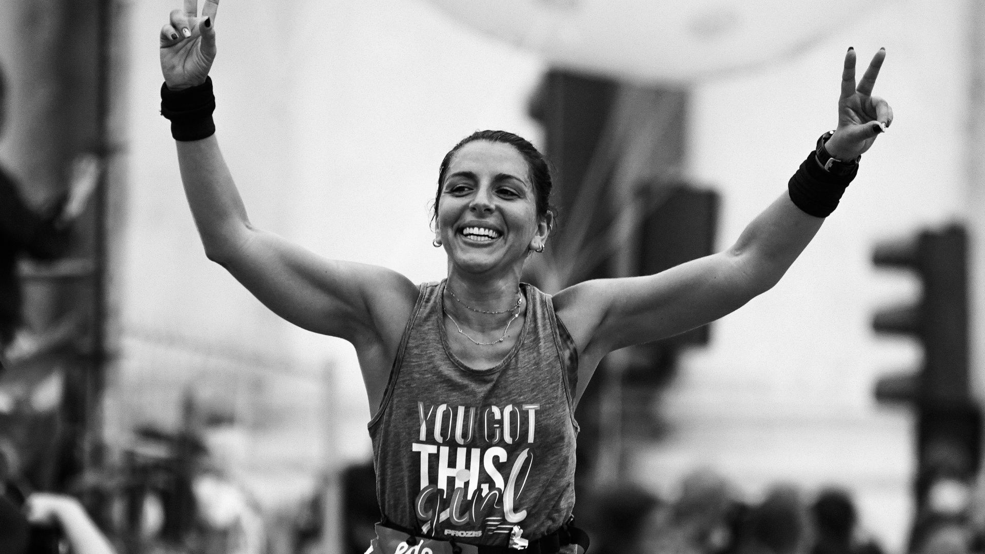 Female runner crossing the finish line with a victorious smile and arms raised in celebration.