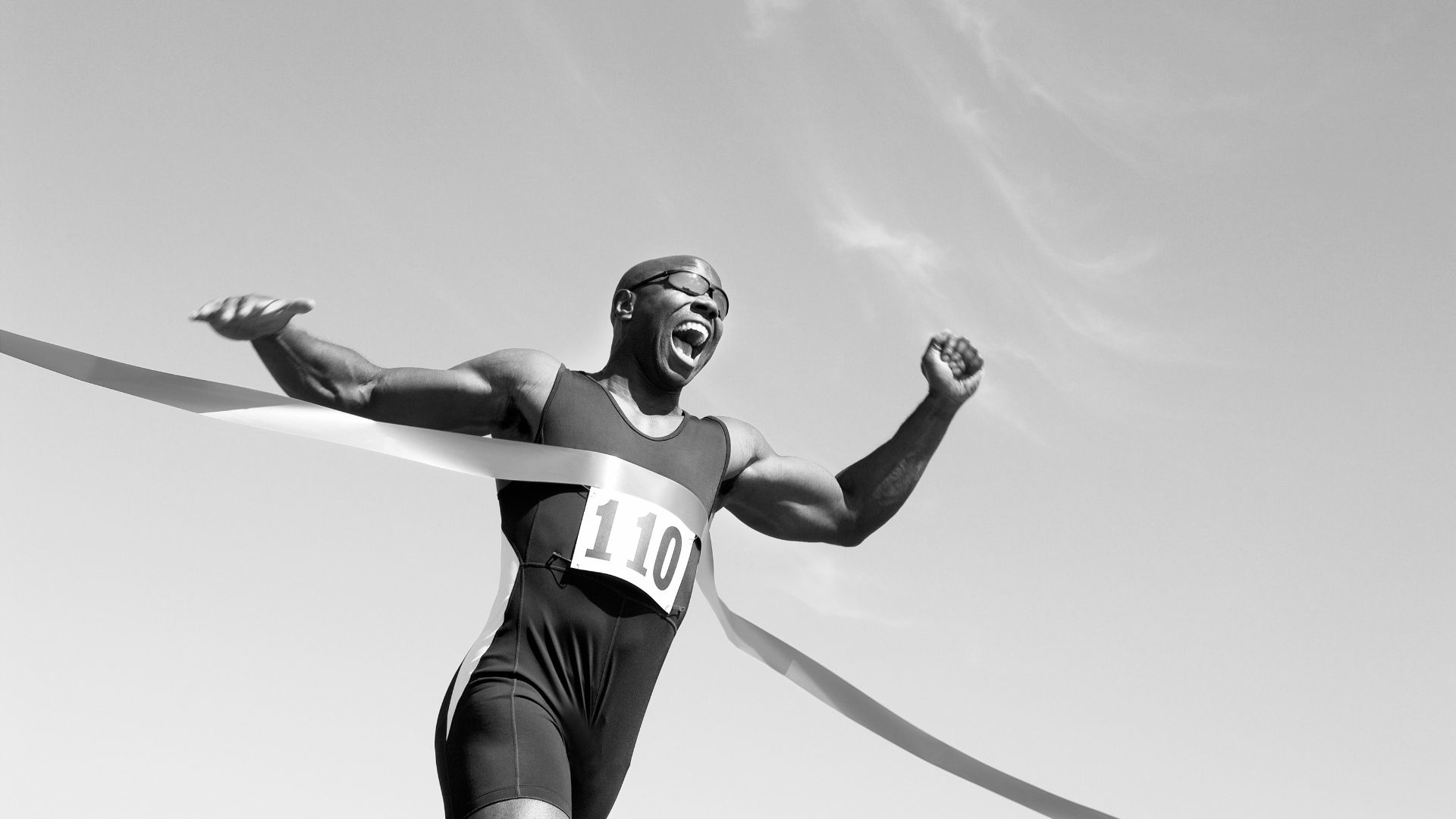 Male runner triumphantly breaking the finish line tape during a race.