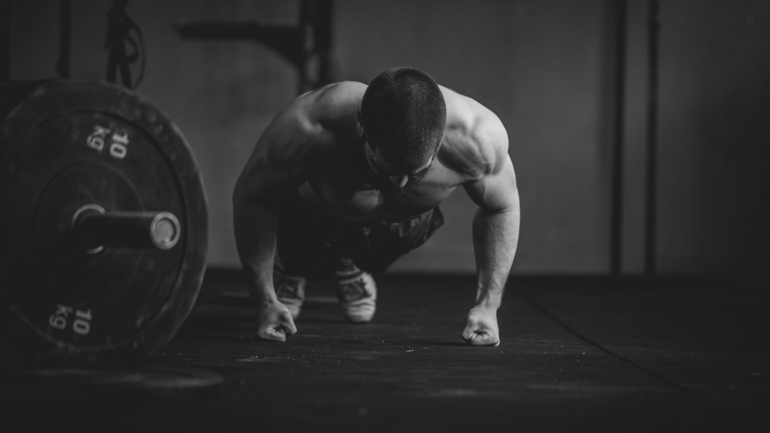 Male athlete performing knuckle pushups next to a loaded barbell during strength conditioning.