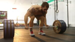 Muscular athlete sets up hip-hinge deadlift form, lats tight and core braced before the pull