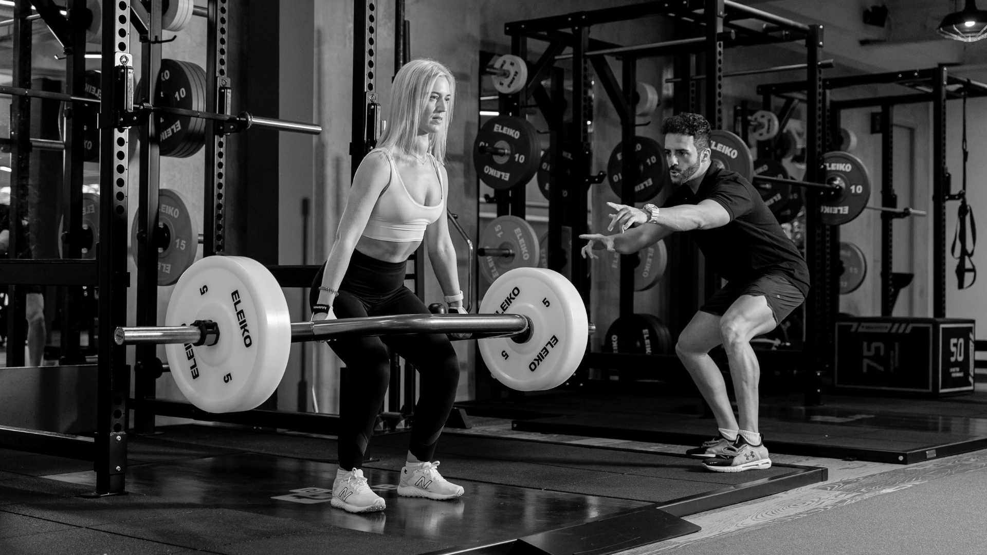 Female lifter practicing sumo deadlift technique under coach’s cue for knee tracking and quad drive