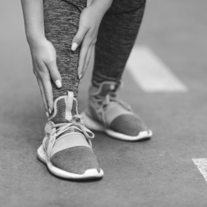 Runner gripping lower shin on the road, demonstrating shin pain during training.
