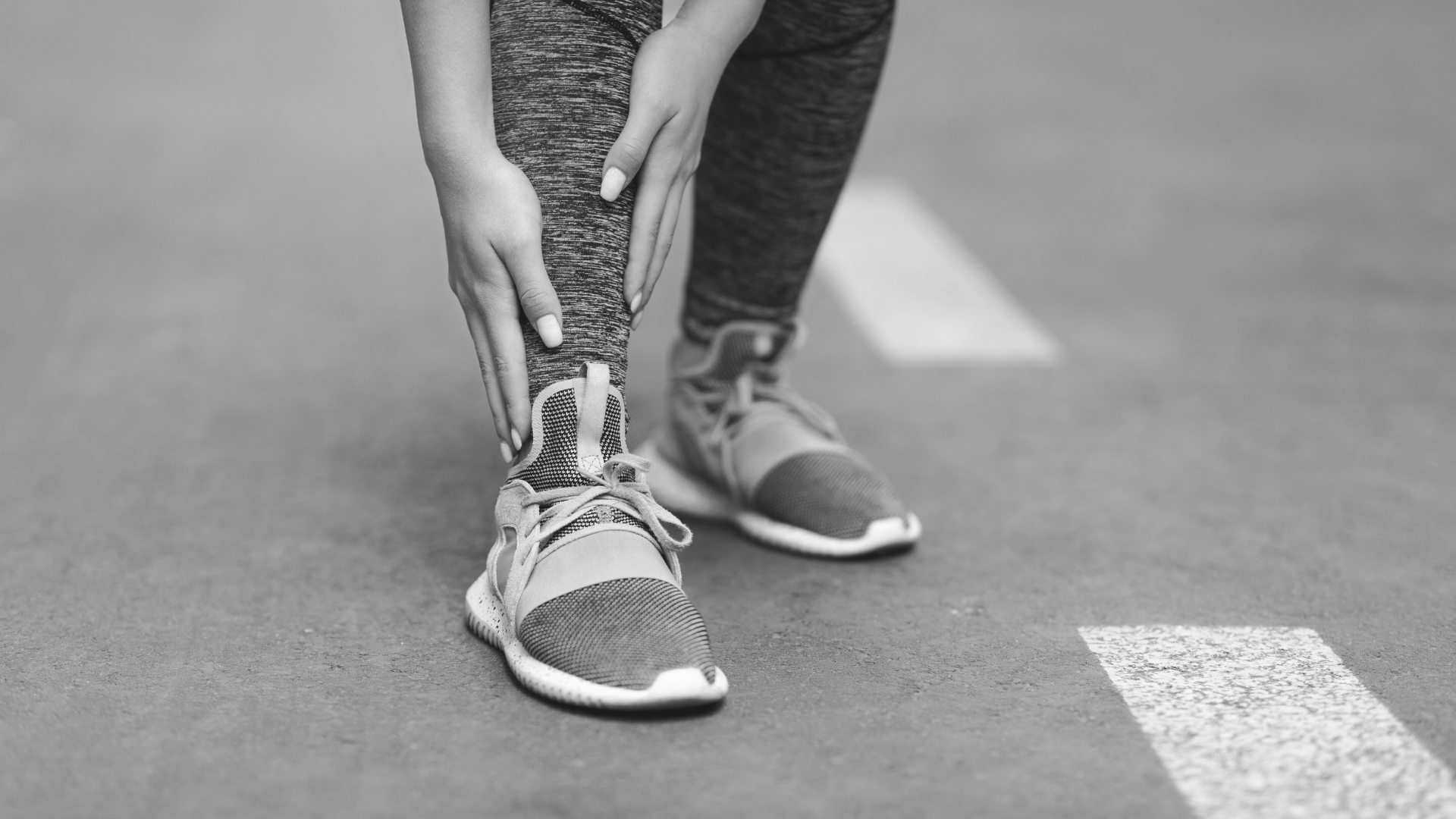 Runner gripping lower shin on the road, demonstrating shin pain during training.